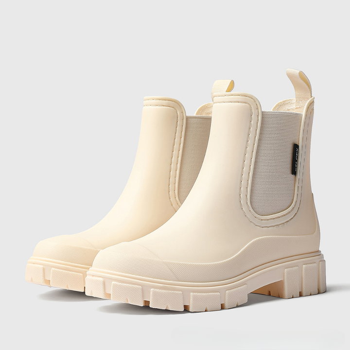 A pair of cream-colored Chelsea boots with chunky lug soles and elastic side panels, shown on a light gray background.