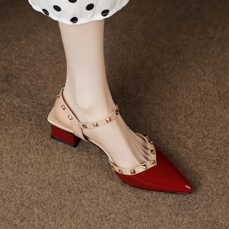 Red pointed-toe shoes with gold studded detail worn by a person on a brown carpet.