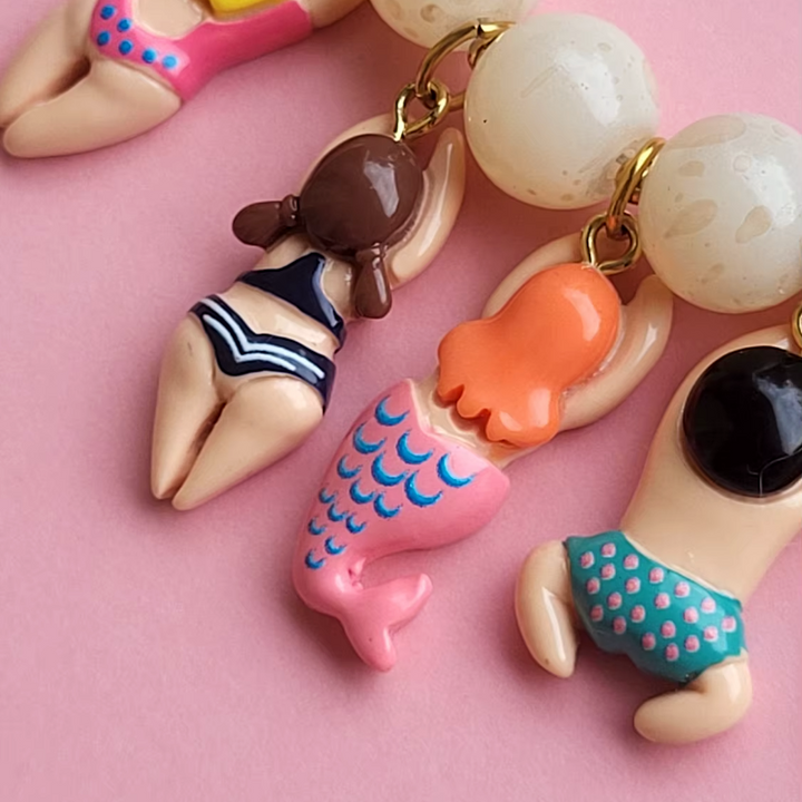 Colorful mermaid-themed keychain charms on a pink background