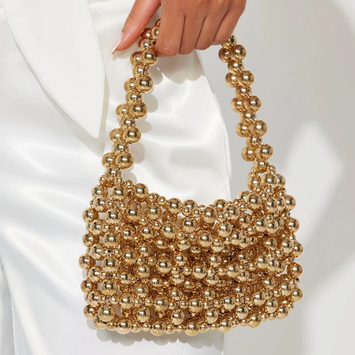 Gold beaded handbag held by a person against a white background