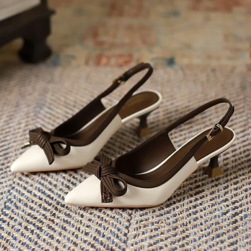 White high-heeled shoes with black bows on a textured surface