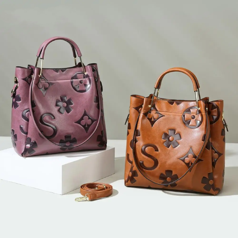 Two handbags, one pink and one brown, with floral and monogram designs on a light gray background.