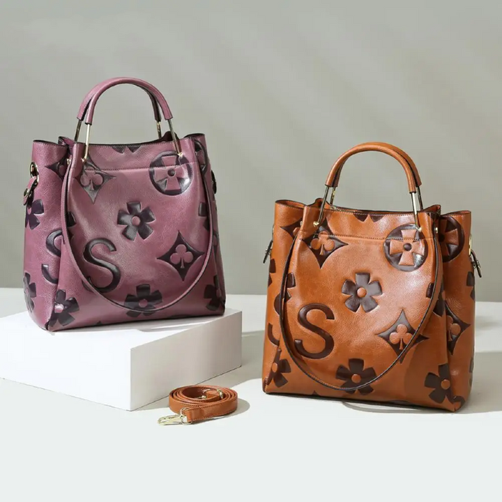 Two handbags, one pink and one brown, with floral and monogram designs on a light gray background.