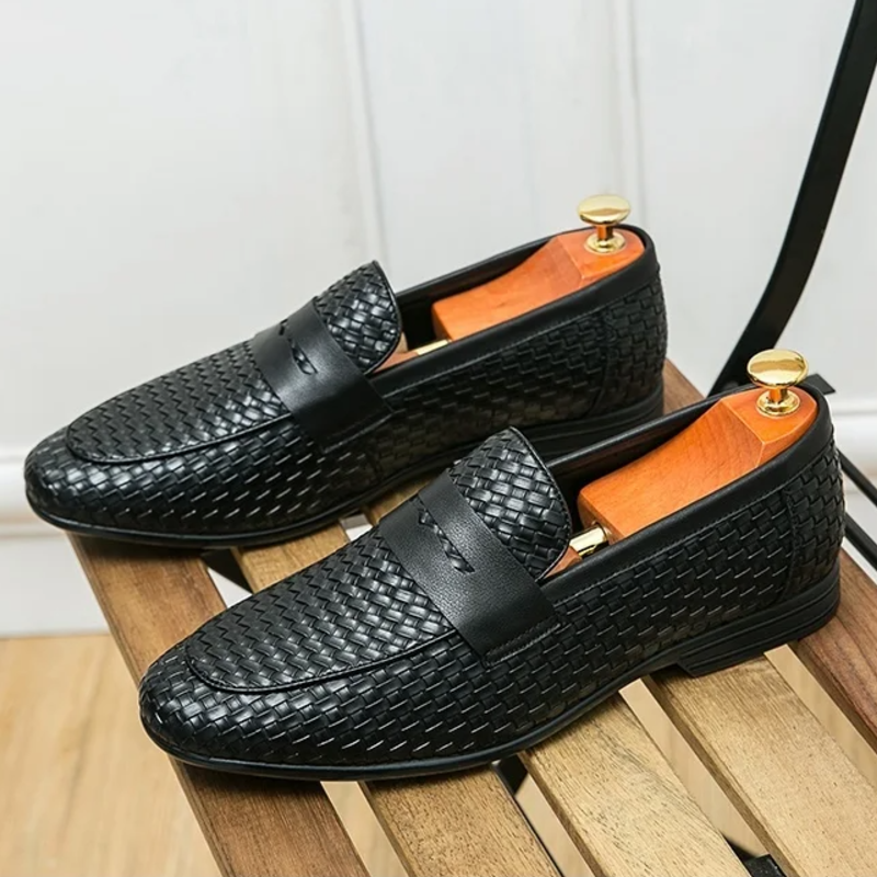 Black textured loafers with gold accents on a wooden surface