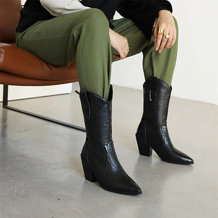 Person wearing black knee-high boots with a textured pattern, sitting on a brown chair.
