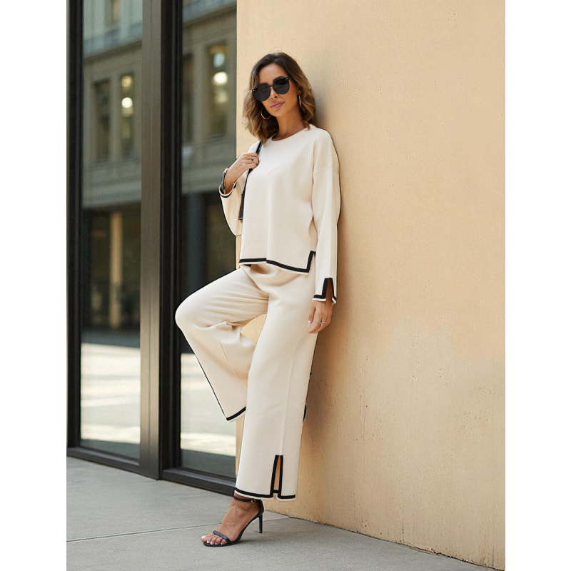 Woman in a white outfit with black accents leaning against a beige wall.
