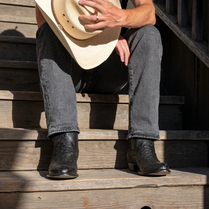 Person wearing a cowboy hat, black boots, and jeans sitting on wooden steps.