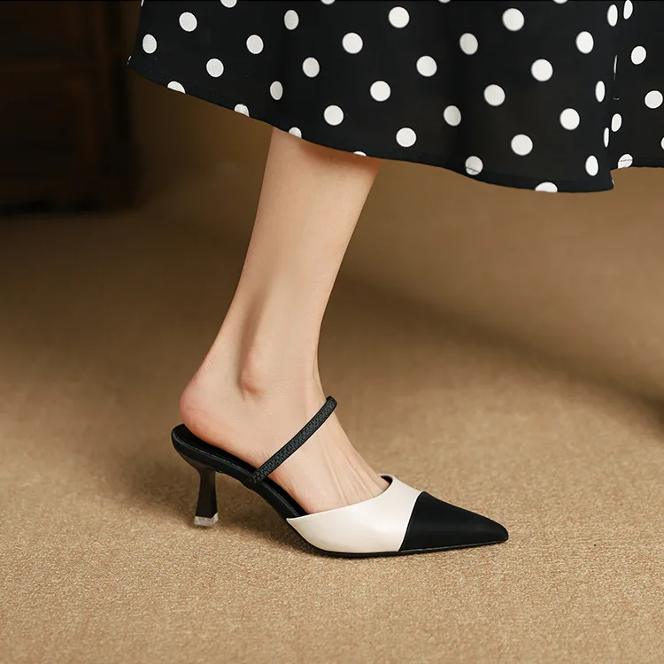 Black and white pointed-toe slingback heels worn with a polka dot skirt on a beige surface.