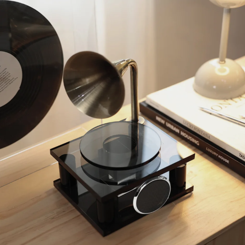 Small black turntable on a wooden surface with a record and books in the background.