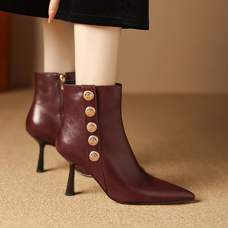 Brown leather ankle boots with gold buttons worn by a person on a beige background
