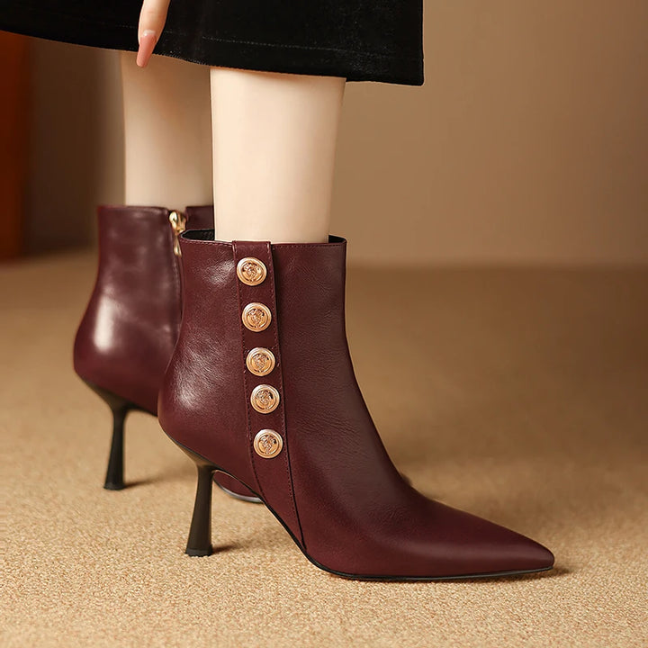 Brown leather ankle boots with gold buttons worn by a person on a beige background