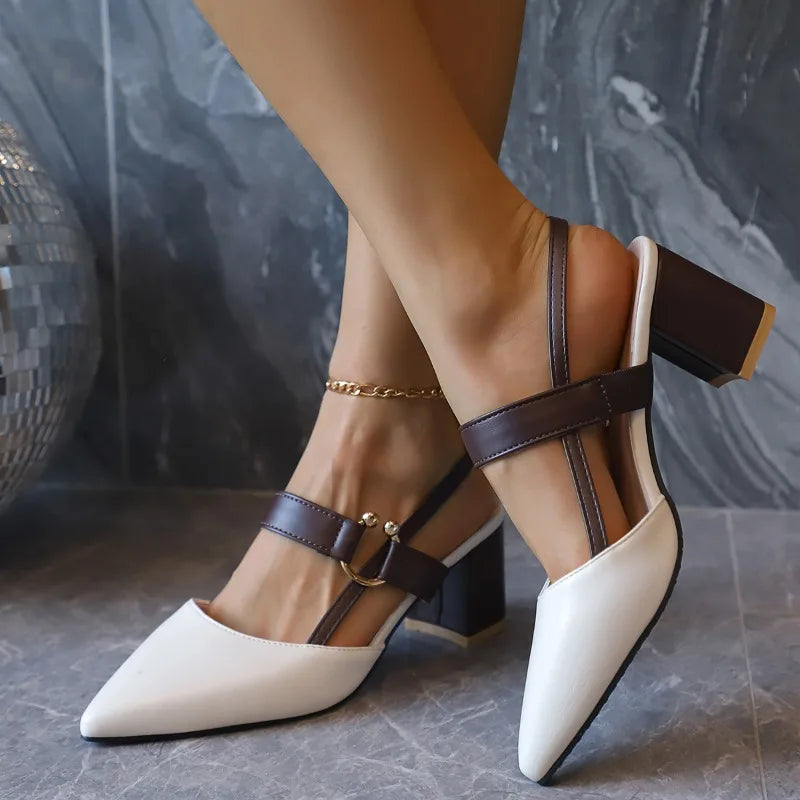 White high-heeled shoes with brown straps worn by a person, against a gray marble background.