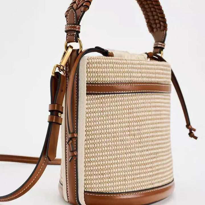 Straw handbag with brown leather accents on a light gray background