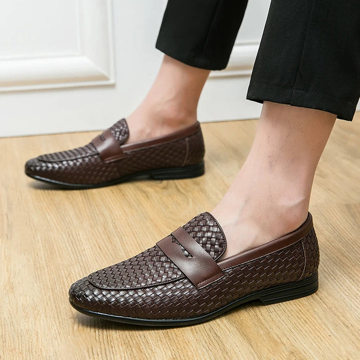 Brown woven loafers worn indoors on a wooden floor.