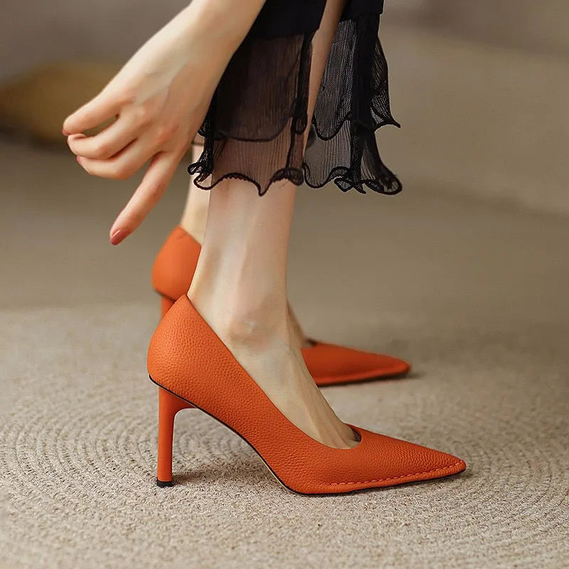 Orange high-heeled shoes worn with a black sheer skirt on a neutral background