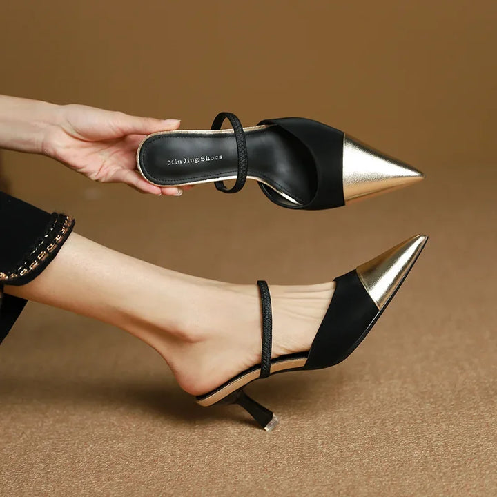 Black high-heeled shoes with gold accents worn by a person on a brown background