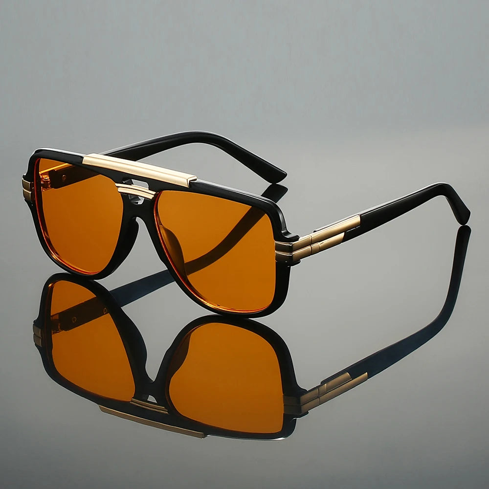Sunglasses with black and gold frame and orange lenses on a reflective gray surface.