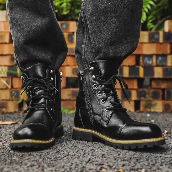 Black leather boots with laces worn by a person standing on a textured surface with wooden blocks in the background.