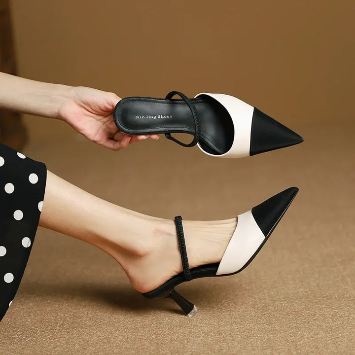 Black and white pointed-toe shoes with a hand holding one shoe on a brown background