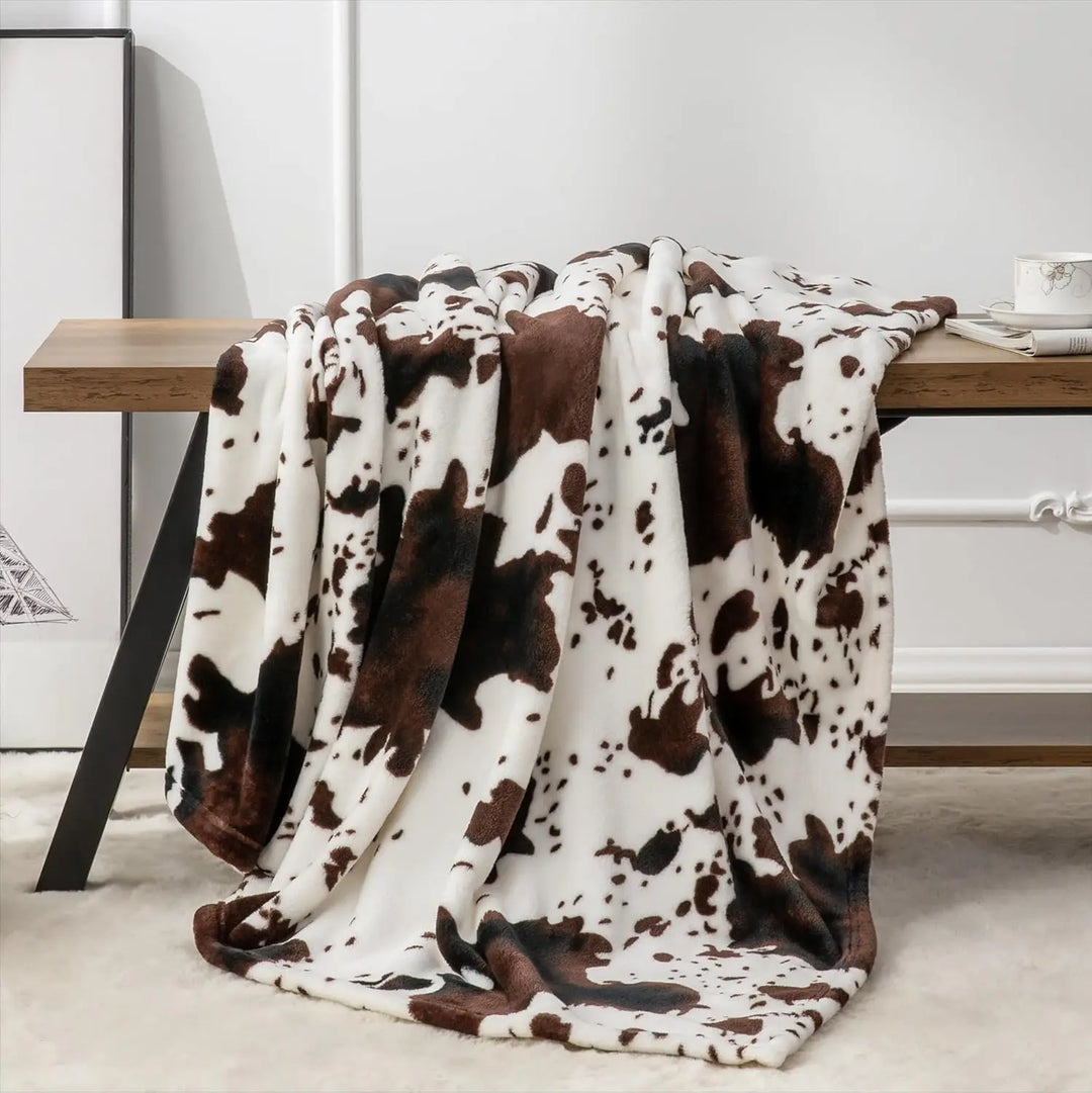 Cow print blanket draped over a wooden bench against a white wall.