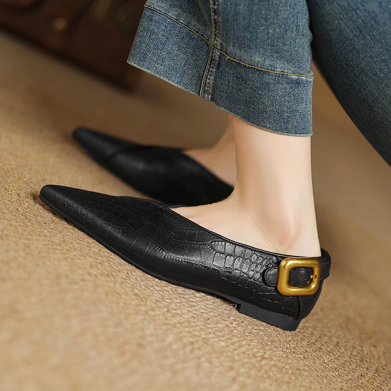 Black pointed-toe flats with a gold buckle on a neutral background