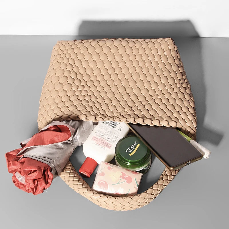 Woven beige bag with various items including a phone, bottle, and cloth on a gray background