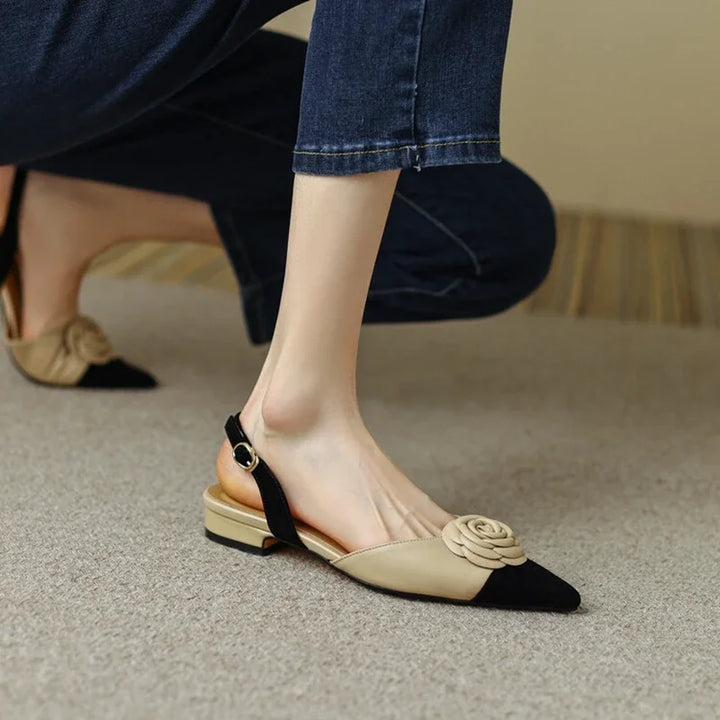 Beige and black flat shoes with a floral design on a neutral background