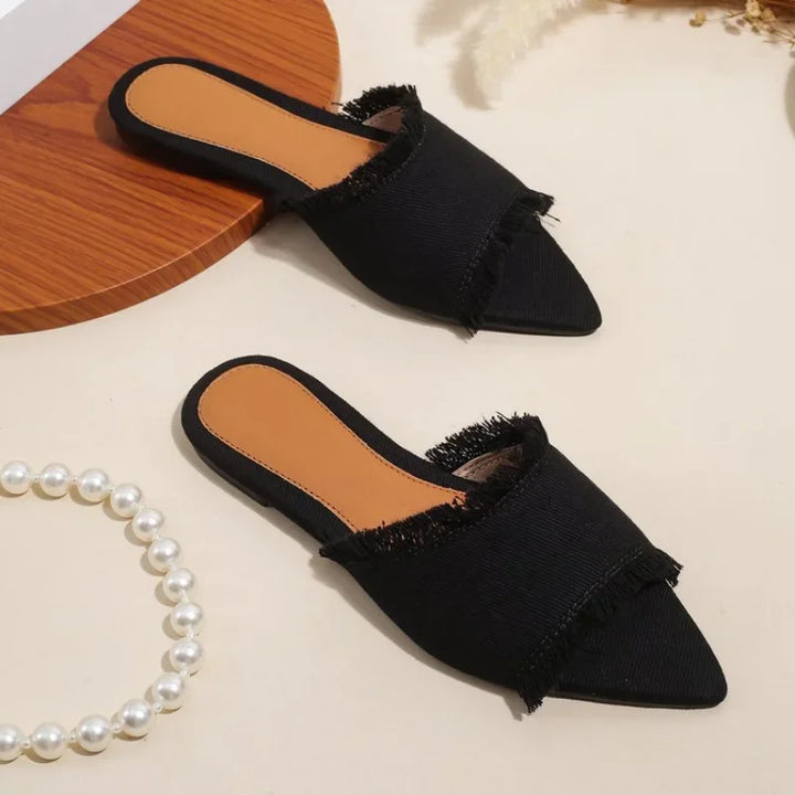 Black pointed-toe slippers with frayed edges on a light background