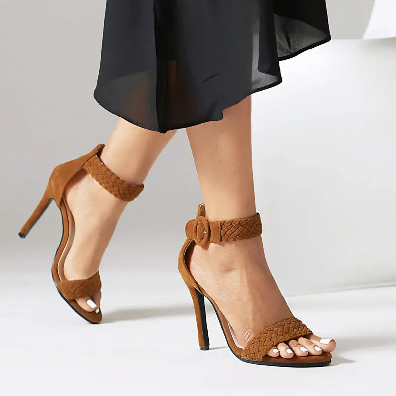 Brown high-heeled sandals with braided straps worn by a person on a white background