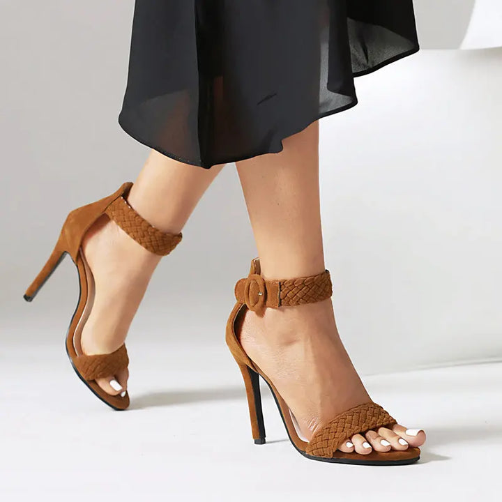 Brown high-heeled sandals with braided straps worn by a person on a white background