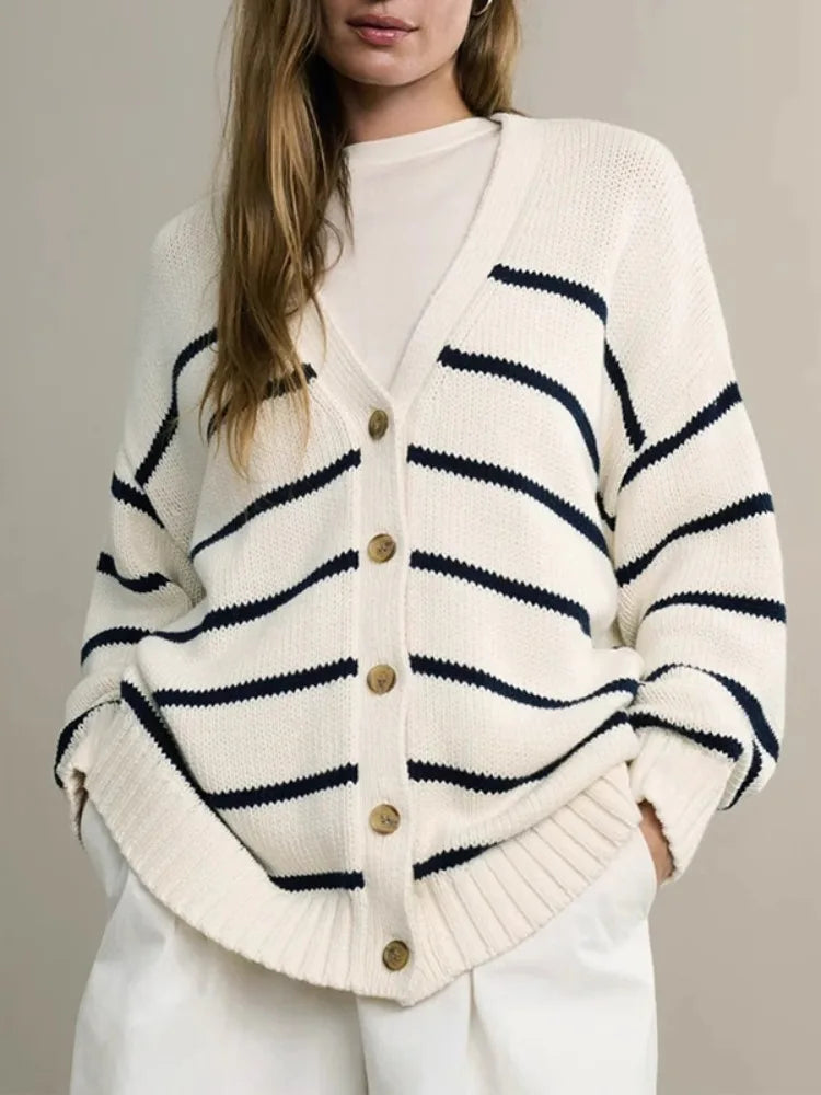 Person wearing a white cardigan with blue stripes and gold buttons on a plain background