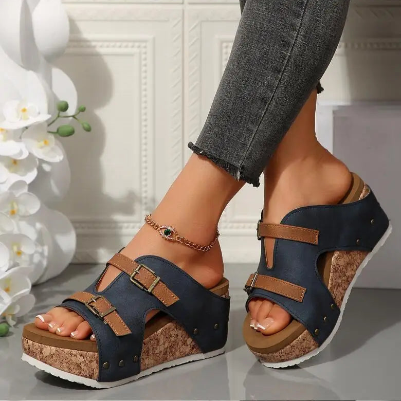 Navy wedge sandals with brown straps worn by a person, with a decorative background.