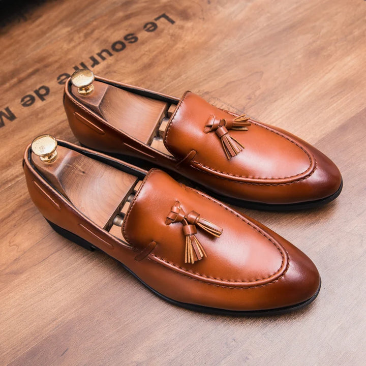 Pair of brown leather loafers with tassels on a wooden surface