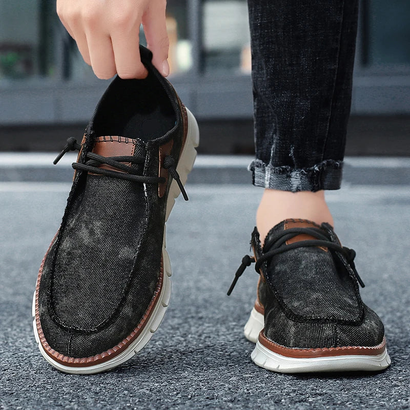 Person wearing black denim shoes with brown accents on a blurred street background