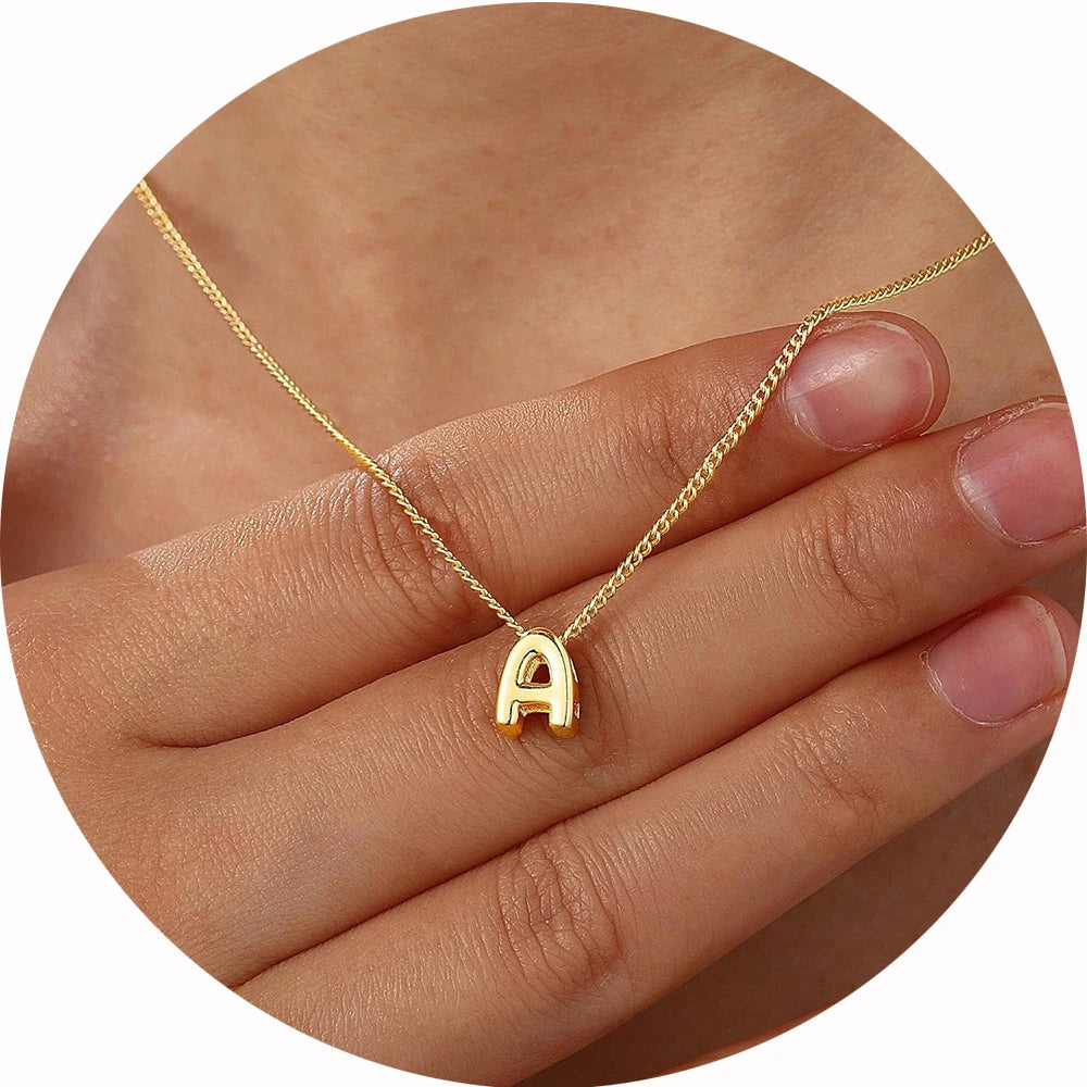 Gold necklace with a 'A' pendant on a hand against a neutral background