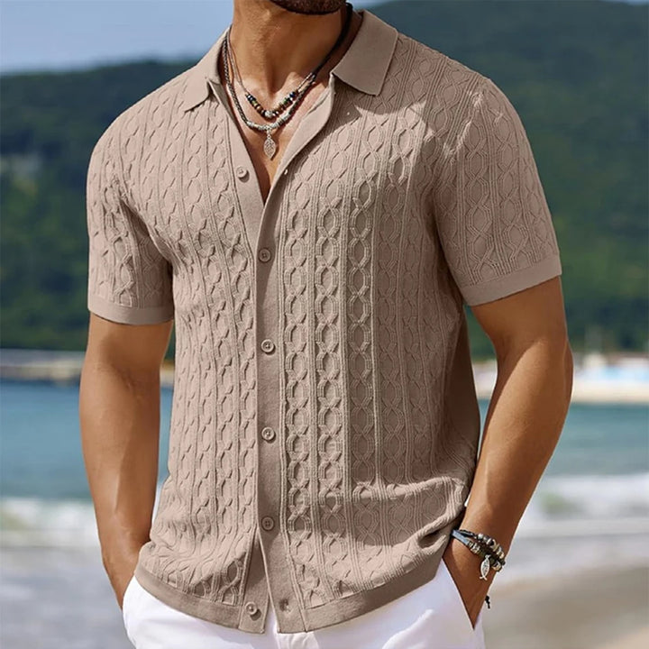 Man wearing a beige cable knit short-sleeve shirt on a beach with blurred background