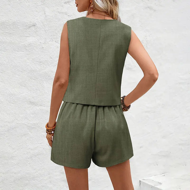Woman wearing a green sleeveless top and shorts set against a white brick wall.