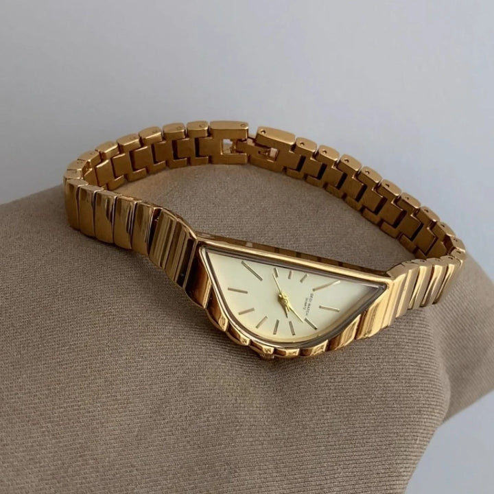 Gold wristwatch on a beige cushion with a light gray background