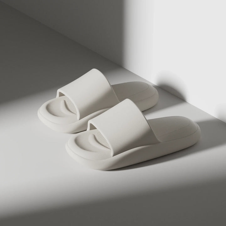 Pair of white slippers on a light gray surface with soft shadows.