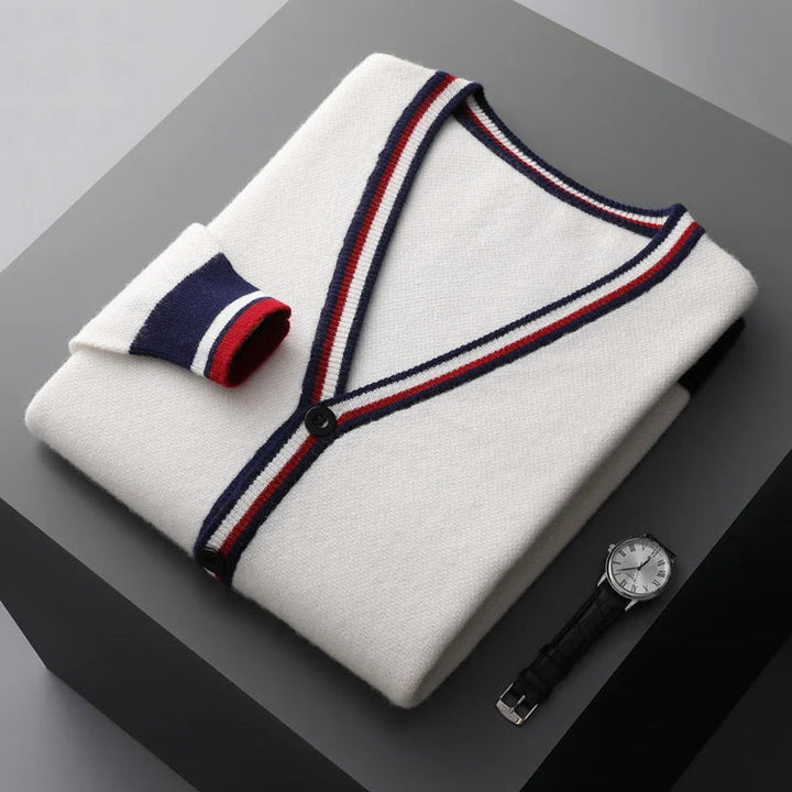 Folded white sweater with red and blue trim on a dark surface, accompanied by a watch.