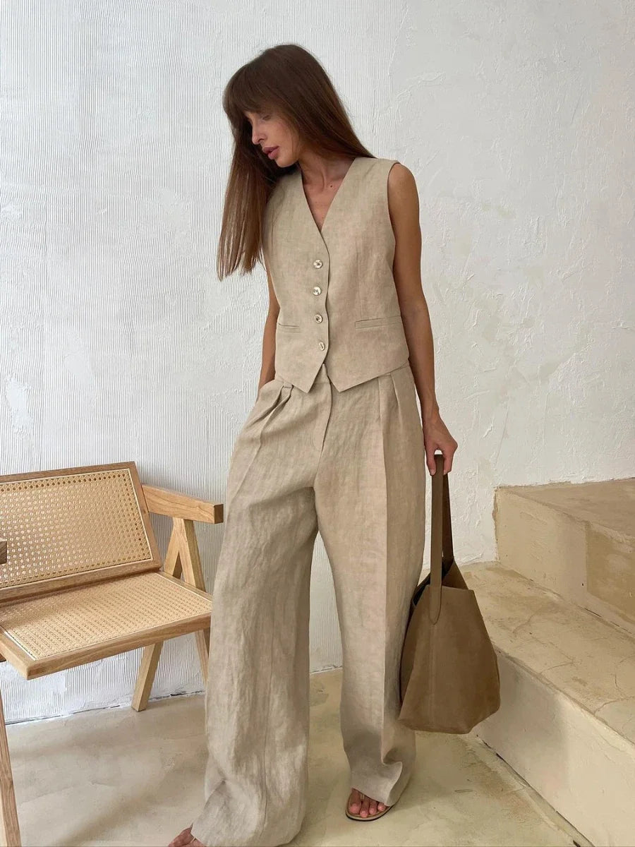 Woman in beige linen suit holding a brown handbag against a white wall.