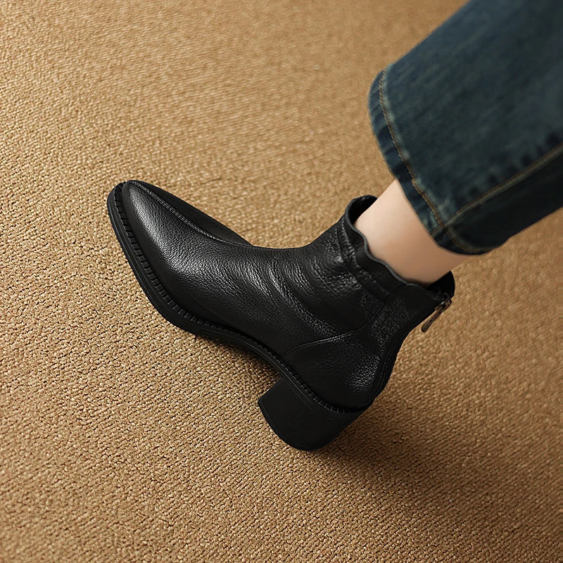 Black leather ankle boot worn on a brown textured surface