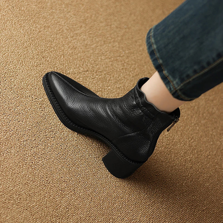 Black leather ankle boot worn on a brown textured surface