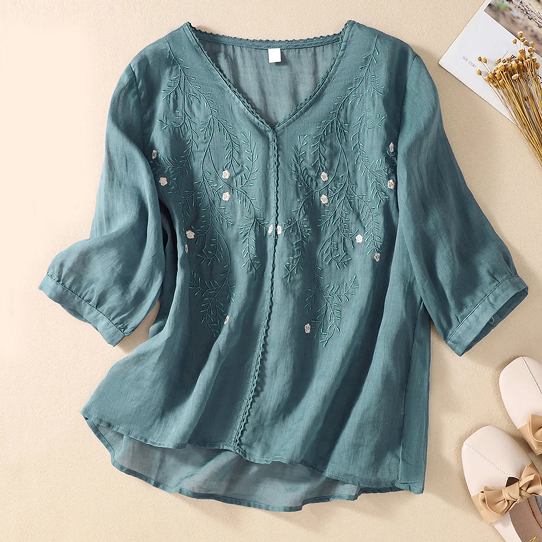 Teal blouse with floral embroidery on a beige background