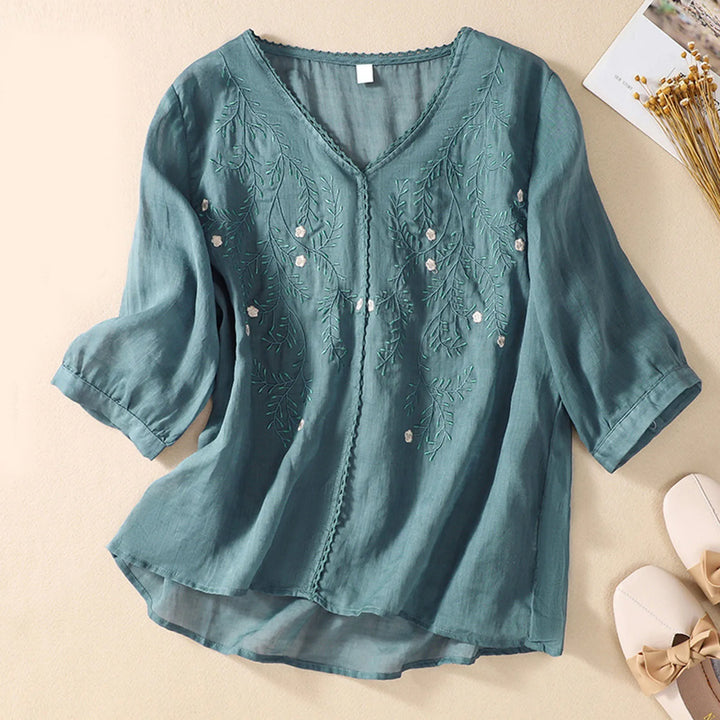 Teal blouse with floral embroidery on a beige background