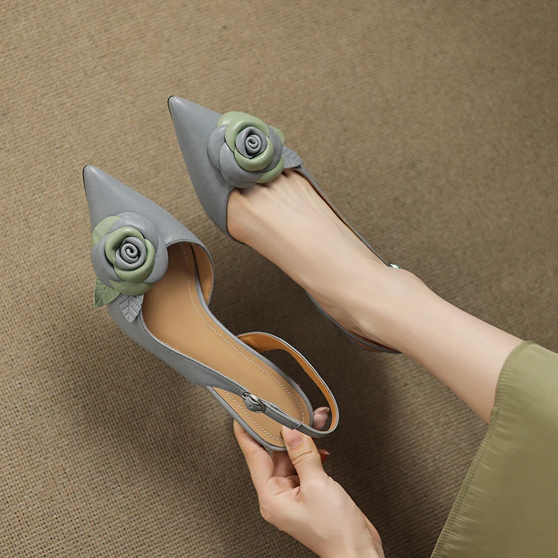 Gray high-heeled shoes with floral decorations held by a hand on a brown background