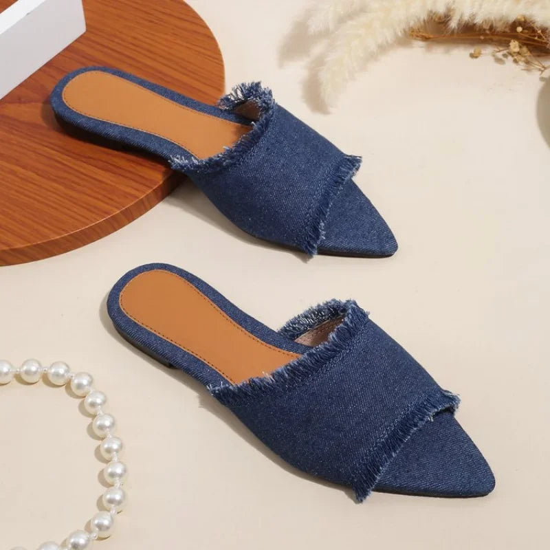 Blue denim slippers on a light beige surface with a pearl necklace.