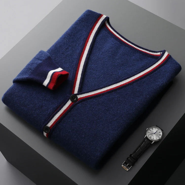 Folded navy blue cardigan with red and white trim on a gray surface, accompanied by a black watch.