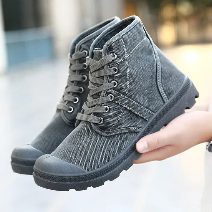 Gray high-top sneakers held by a hand with a blurred background