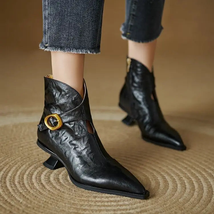 Black leather boots with gold buckles worn by a person on a beige carpet.